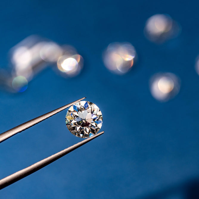 Close Up of Tweezer Holding a Lab Grown Diamond with Moissanite Gems on the Background